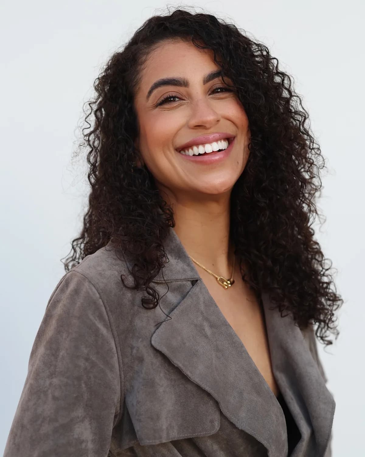 Rossy M. Peralta smiling in a soft taupe blazer against a white studio backdrop
