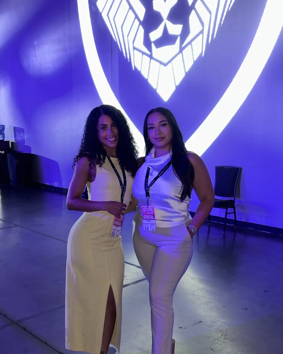 Two members photographed against the Alpha Society backdrop